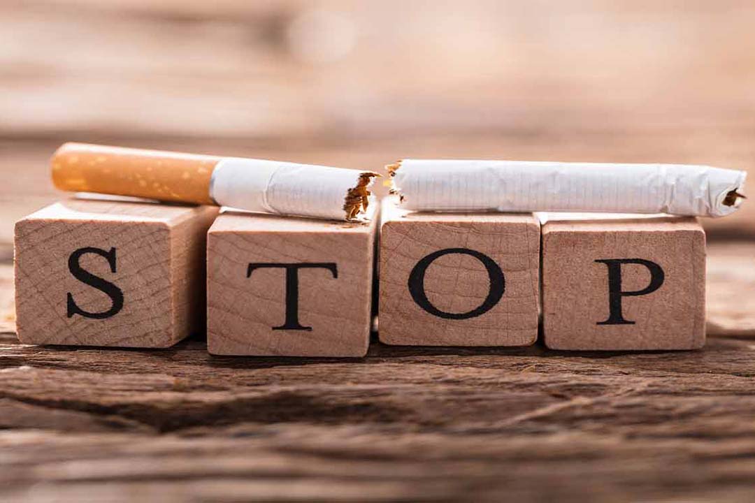 4 Holzwürfel bilden das Wort Stop und auf ihnen liegt eine zerbrochene Zigarette