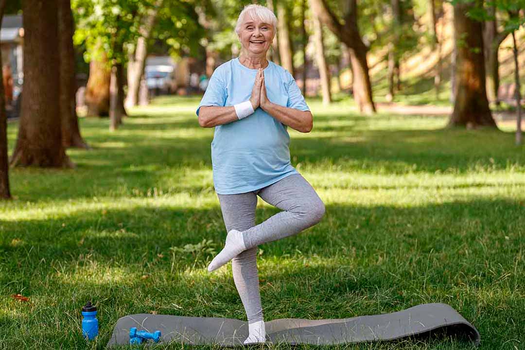 Eine ältere Frau in Sportbekleidung macht im Grünen eine Yogaübung
