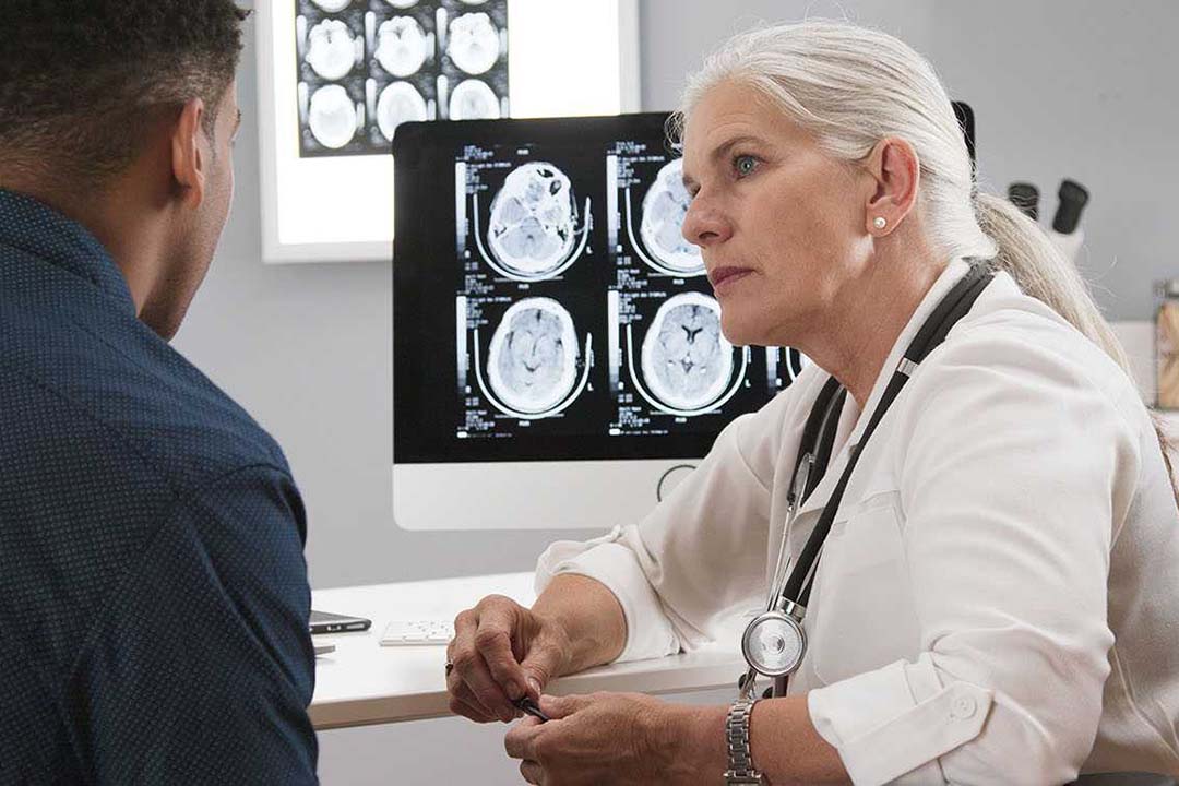 Beratungsgespräck mit einer Ärztin, im Hintergrund sind Bilder eines Schädelscans zu sehen