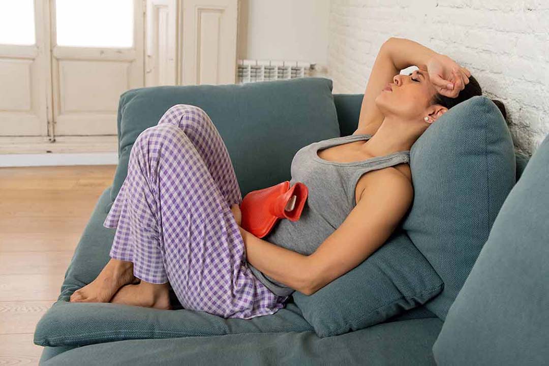 Eine Frau auf einer Couch mit einer Wärmflasche auf dem Bauch
