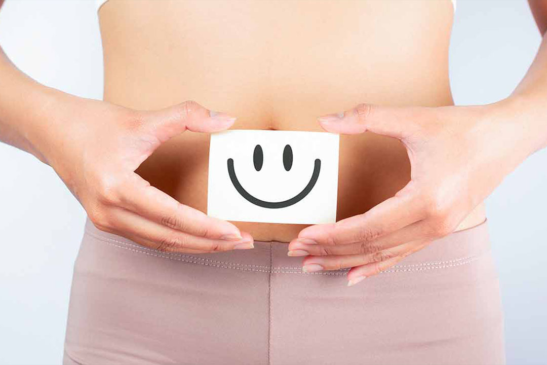 Frau hält sich einen Zettel mit lachendem Smiley vor ihren Bauchnabel