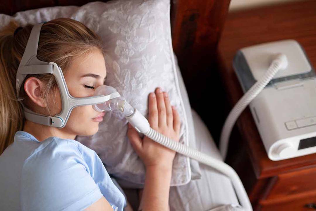 Eine Frau liegt in Seitenlage im Bett und trägt eine Nasen Atemmaske