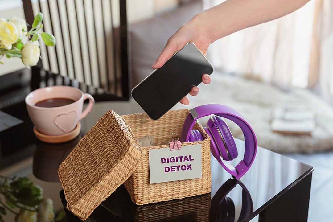 Eine Frau legt ihr Handy in einen Korb mit der Aufschrift Digital Detox