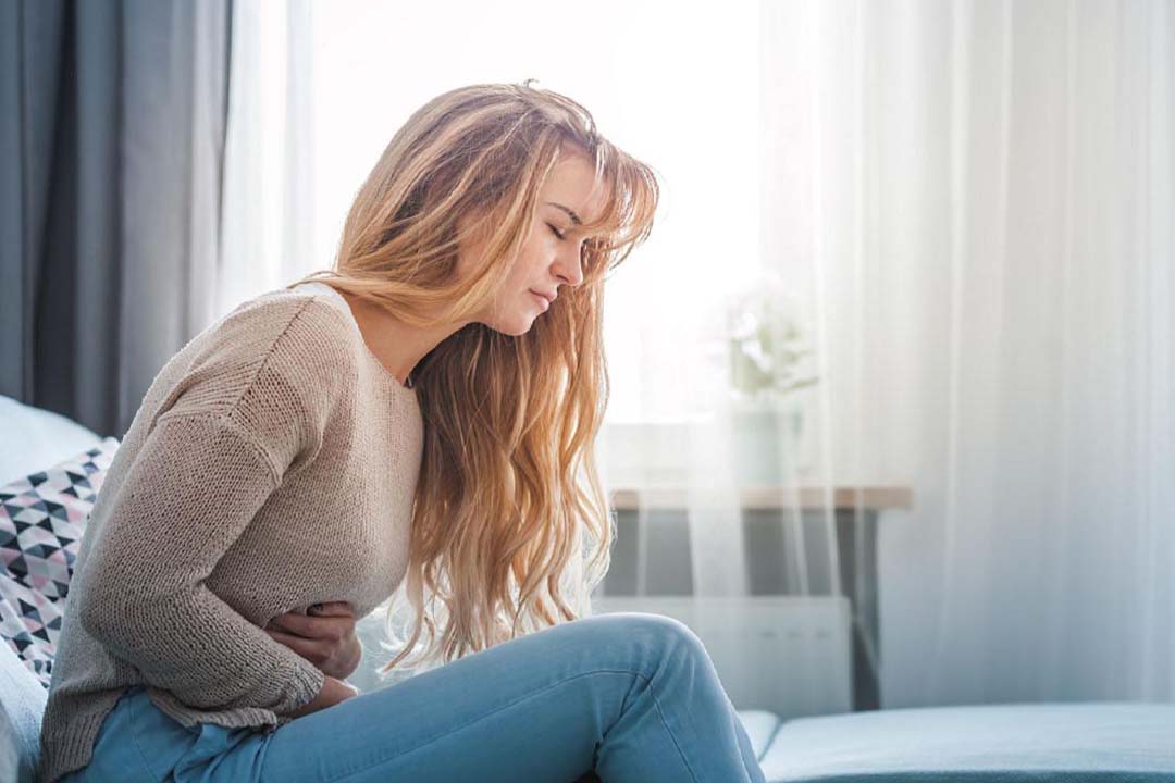 Frau sitzt mit Schmerzen auf dem Sofa