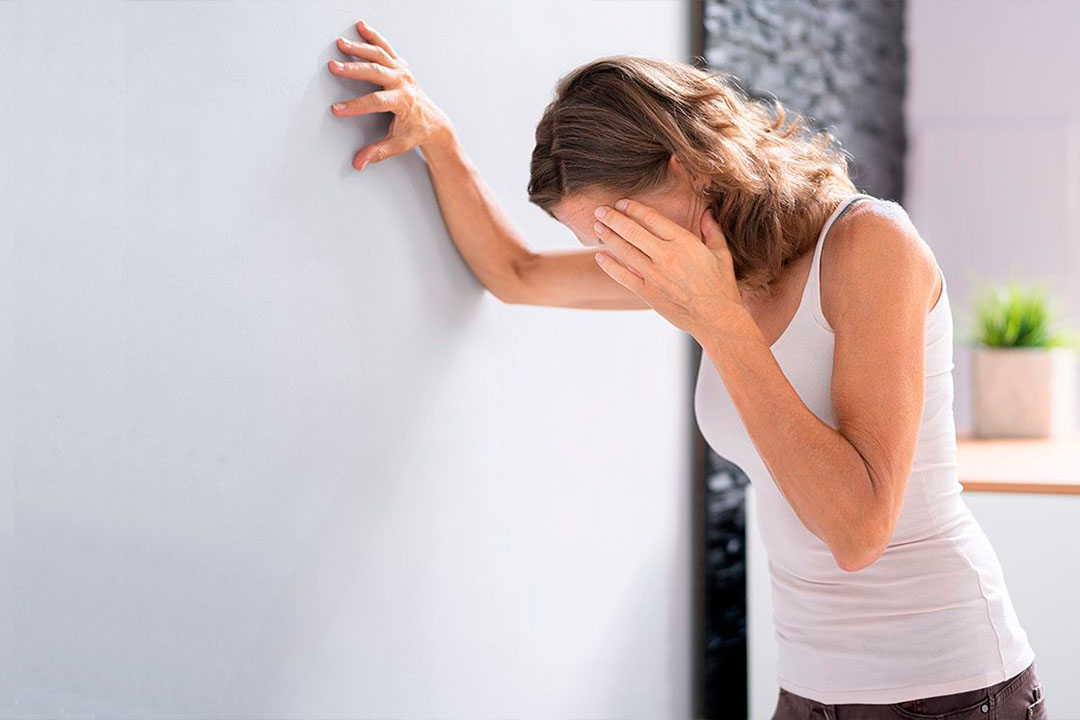 Frau mit Schwächeanfall lehnt sich an eine Wand