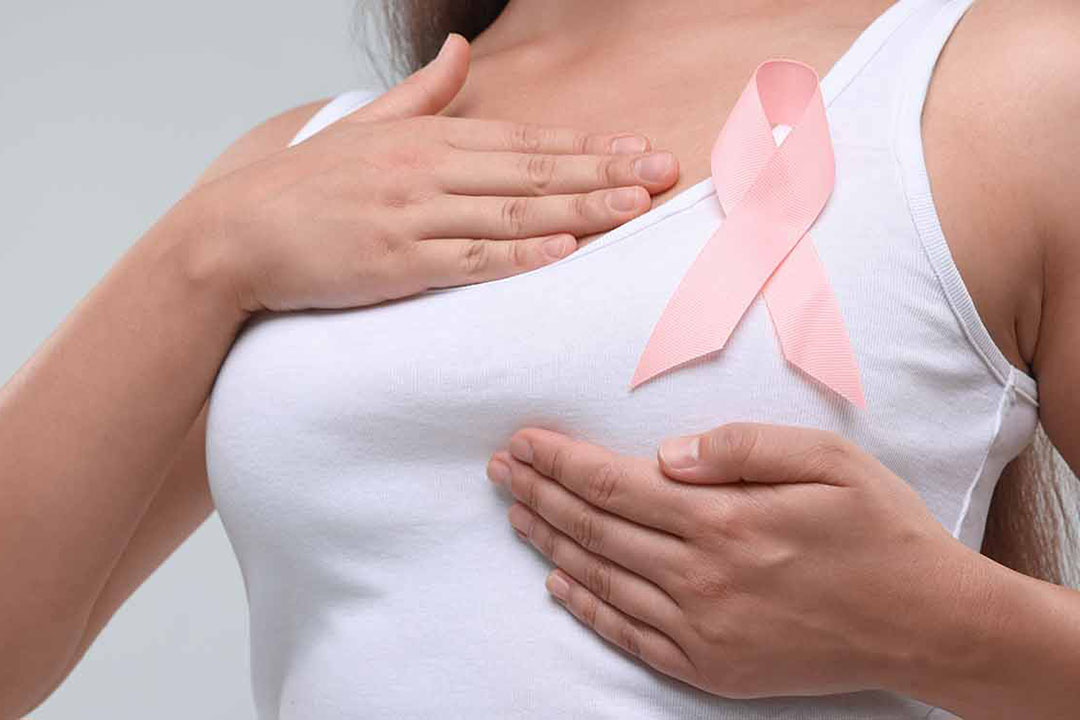 Eine Frau in einem Weißen Shirt mit Rosa schleife tastet ihre Brust ab