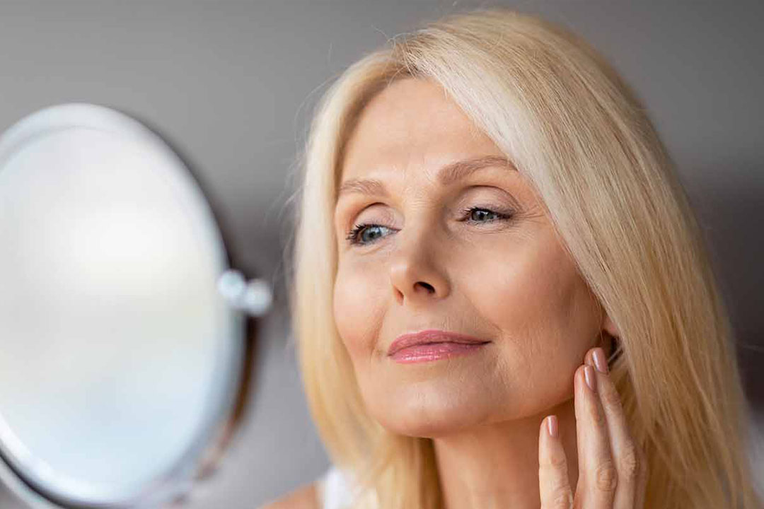 Frau schaut sich im Spiegel an und berührt ihr Gesicht