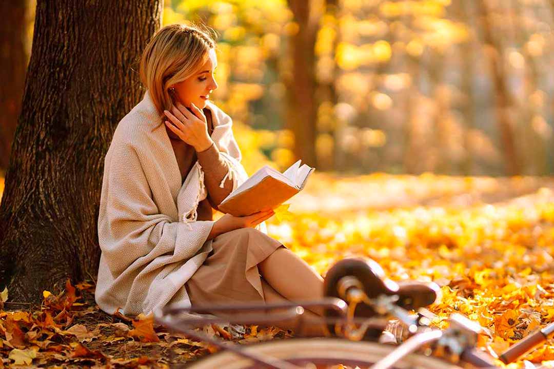 Eine Frau sitzt im Wald an einem Baum ein Buch lesend