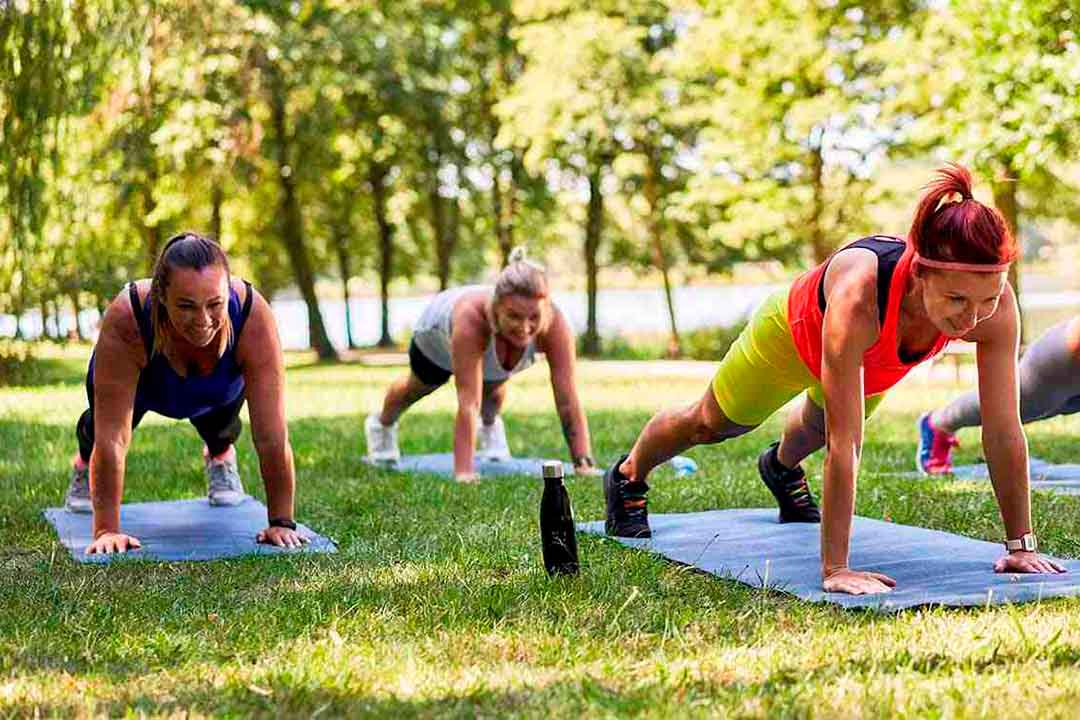 Vier Frauen in Sportbekleidung machen  im Park Liegestuetzen auf Sportmatten