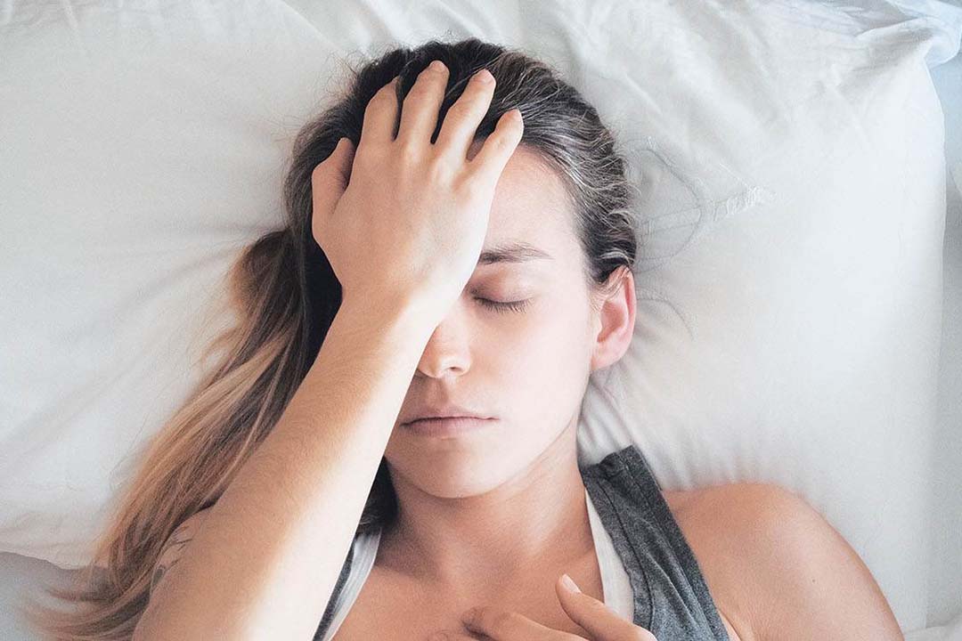 Eine junge Frau liegt im Bett und drückt sich die Stirn