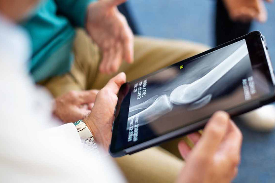 Arzt mit einem Tablet das eine Röntgenaufnahme eines Kniegelenks zeigt