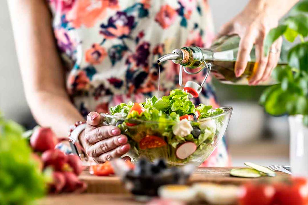 Eine Frau gießt Öl auf einen Salat