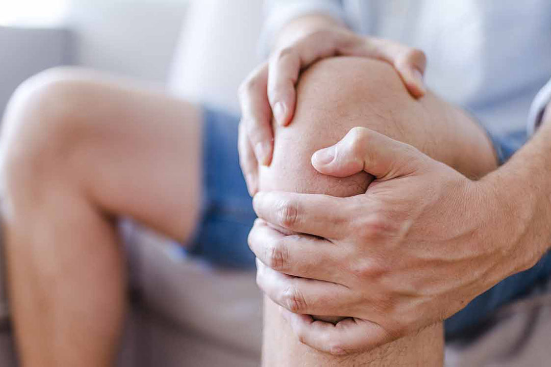 Mann umfasst mit seinen Händen das schmerzende Knie