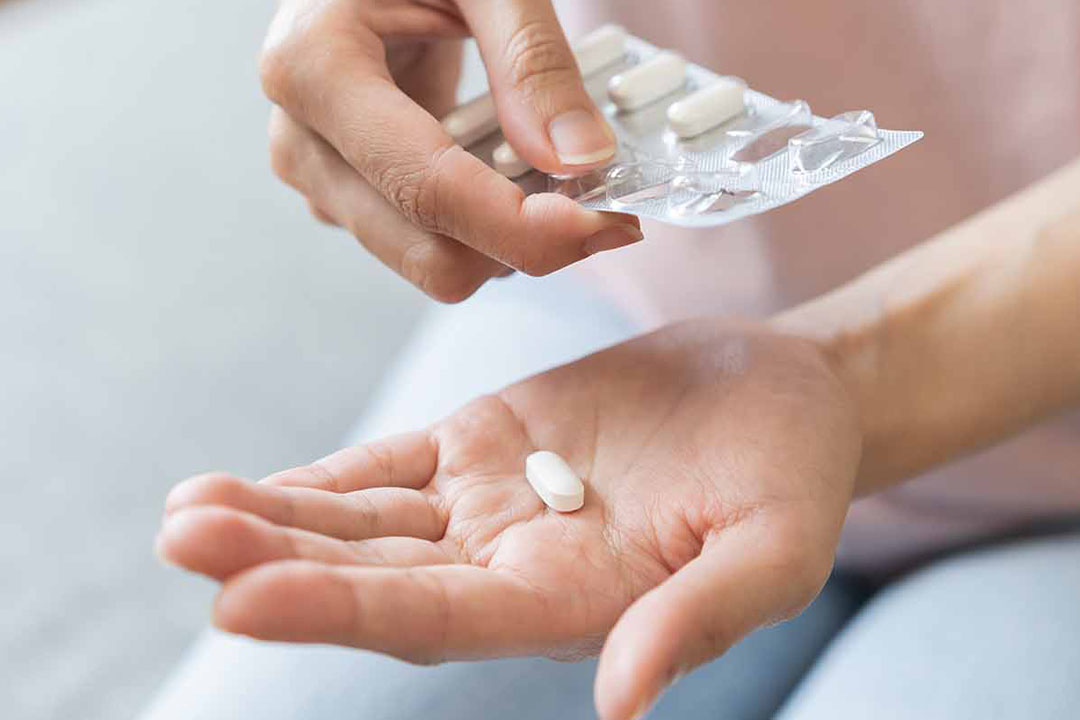 Nahaufnahme Hand mit Tablettenblister und Hand mit Tablette