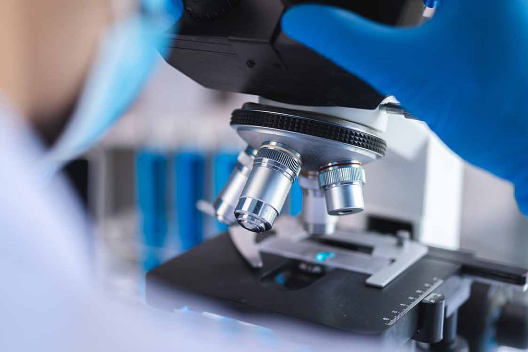 Nahaufnahme einer Person die durch ein Mikroskop schaut