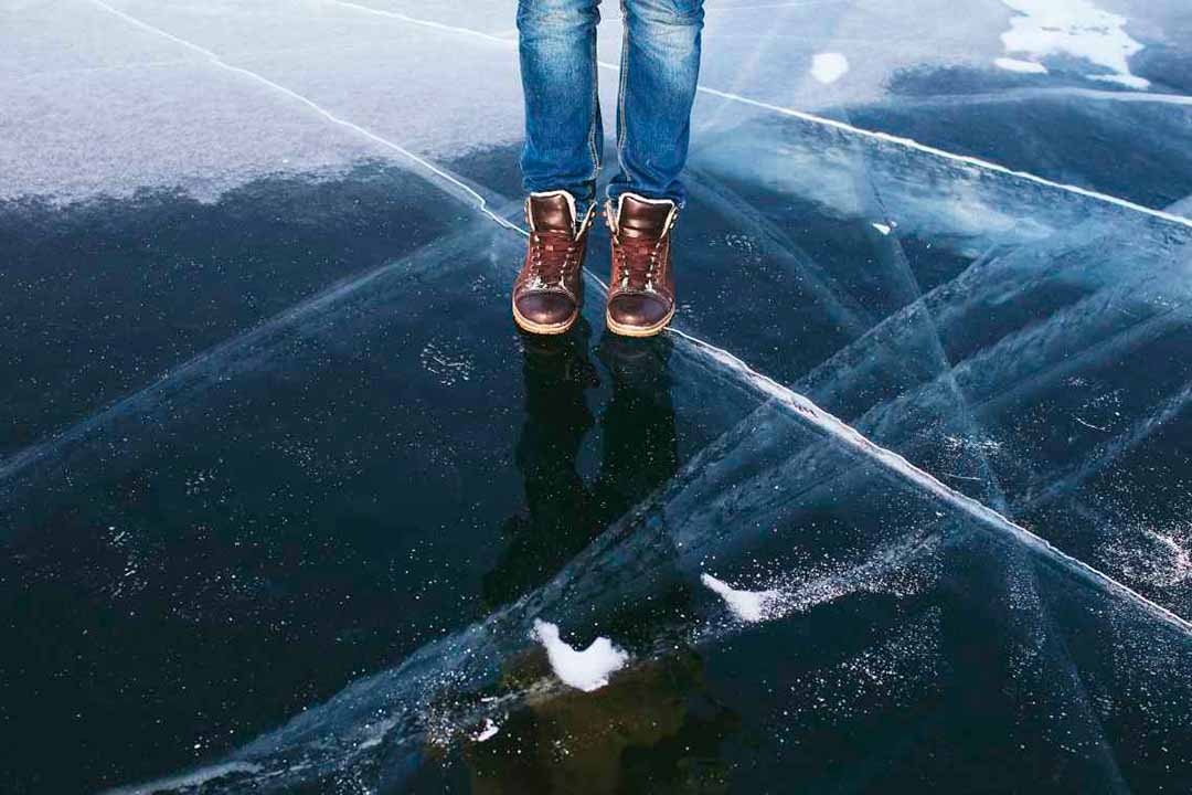 Es sind Füße einer Person zu sehen, die auf einer dicken Eisschicht steht.