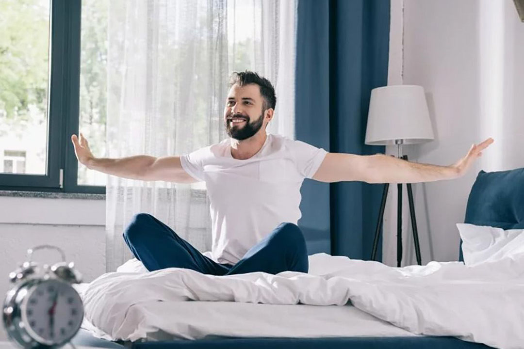 Ein Mann sitzt auf dem Bett und streckt beide Arme zur Seite