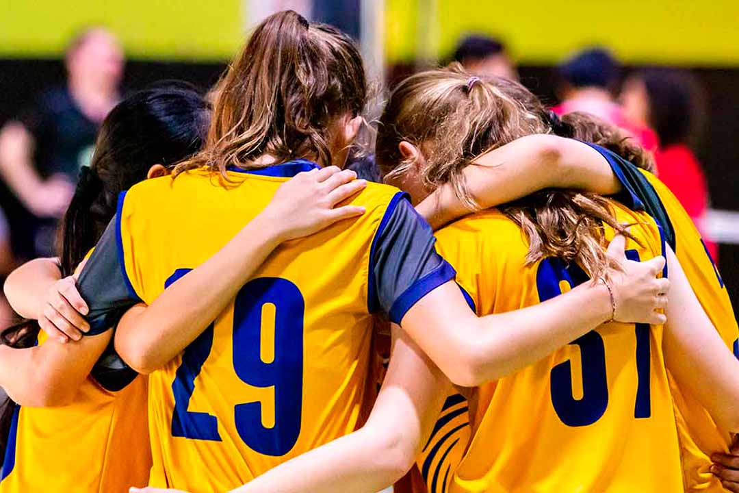 Volleyballerinnen mit gelben Trikots stehen im Kreis und umarmen sich