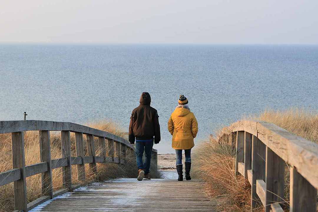 Zwei Menschen gehen auf einem Steg zum Meer