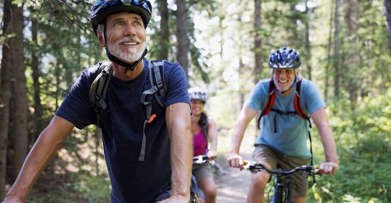 3 Personen mit Fahrradhelm machen eine Radtour durch den Wald