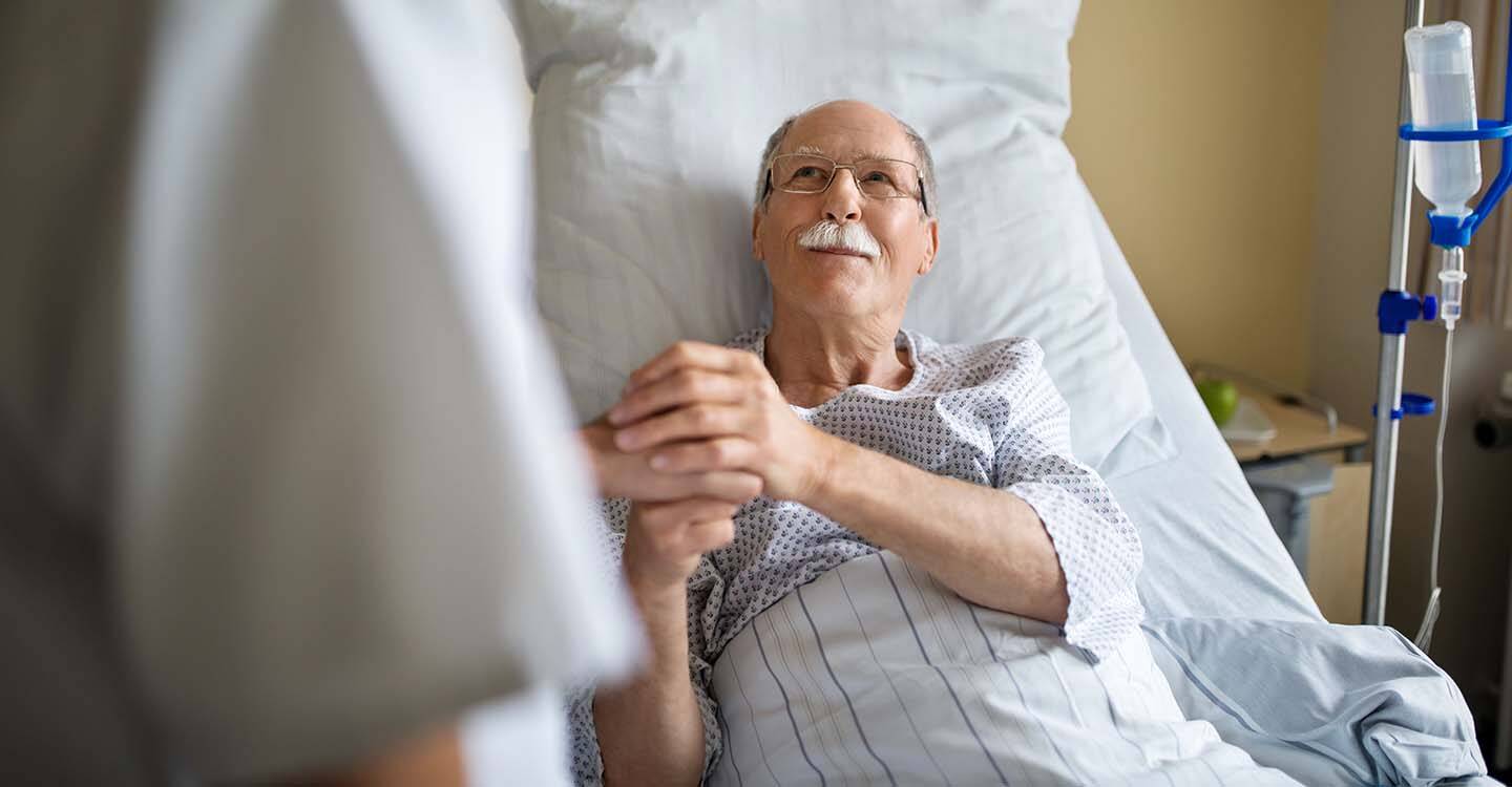 Ein älterer Mann liegt im Krankenbett und hält die Hand eines Arztes