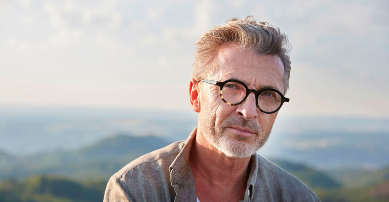 Älterer Mann mit Brille vor einer Hügellandschaft