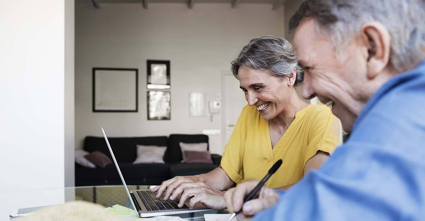 Ein älteres Paar füllt lachend ein Formular am Laptop aus