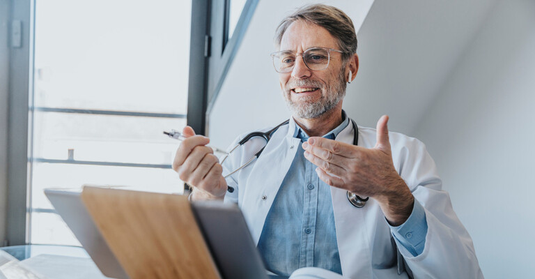 Ein Arzt sitzt am Schreibtisch vor einem Tablet
