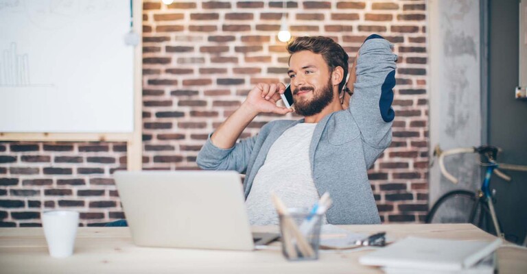 Ein bärtiger Mann sitzt am Schreibtisch und telefoniert