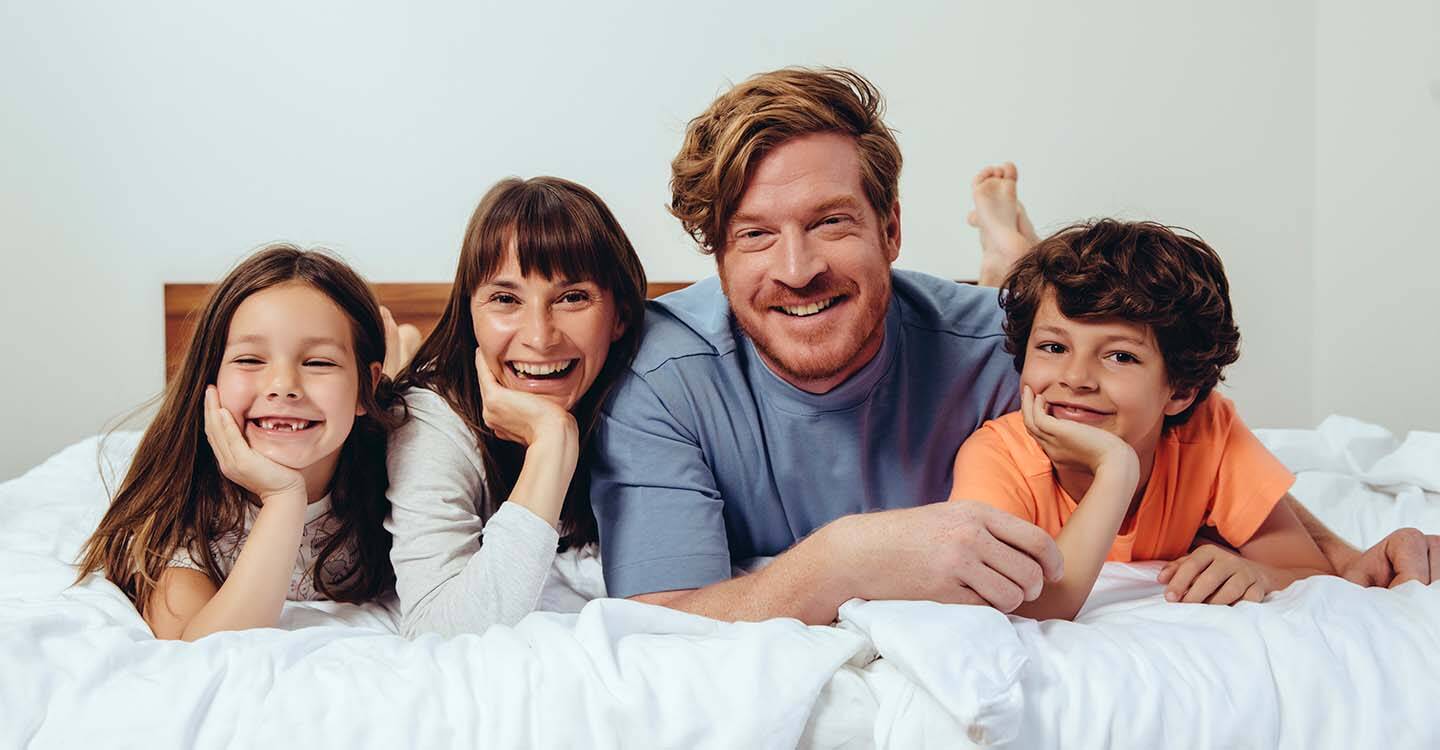 Eine Familie liegt auf einem Bett und schaut in die Kamera