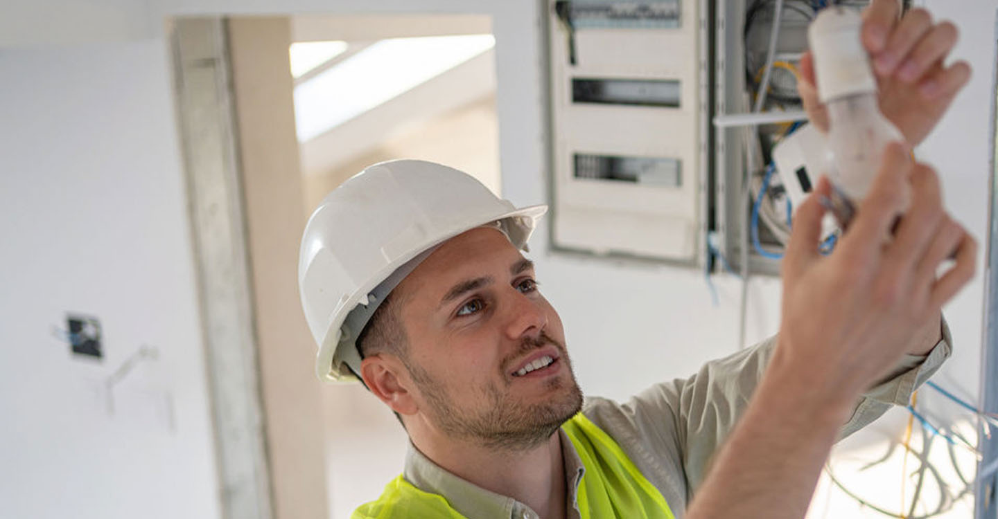 Elektroinstallateur Tim mit Schutzhelm arbeitet an einer Glühbirne