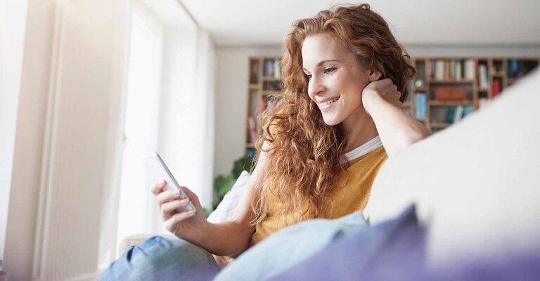 Eine junge Frau mit ihrem Smartphone auf dem Sofa