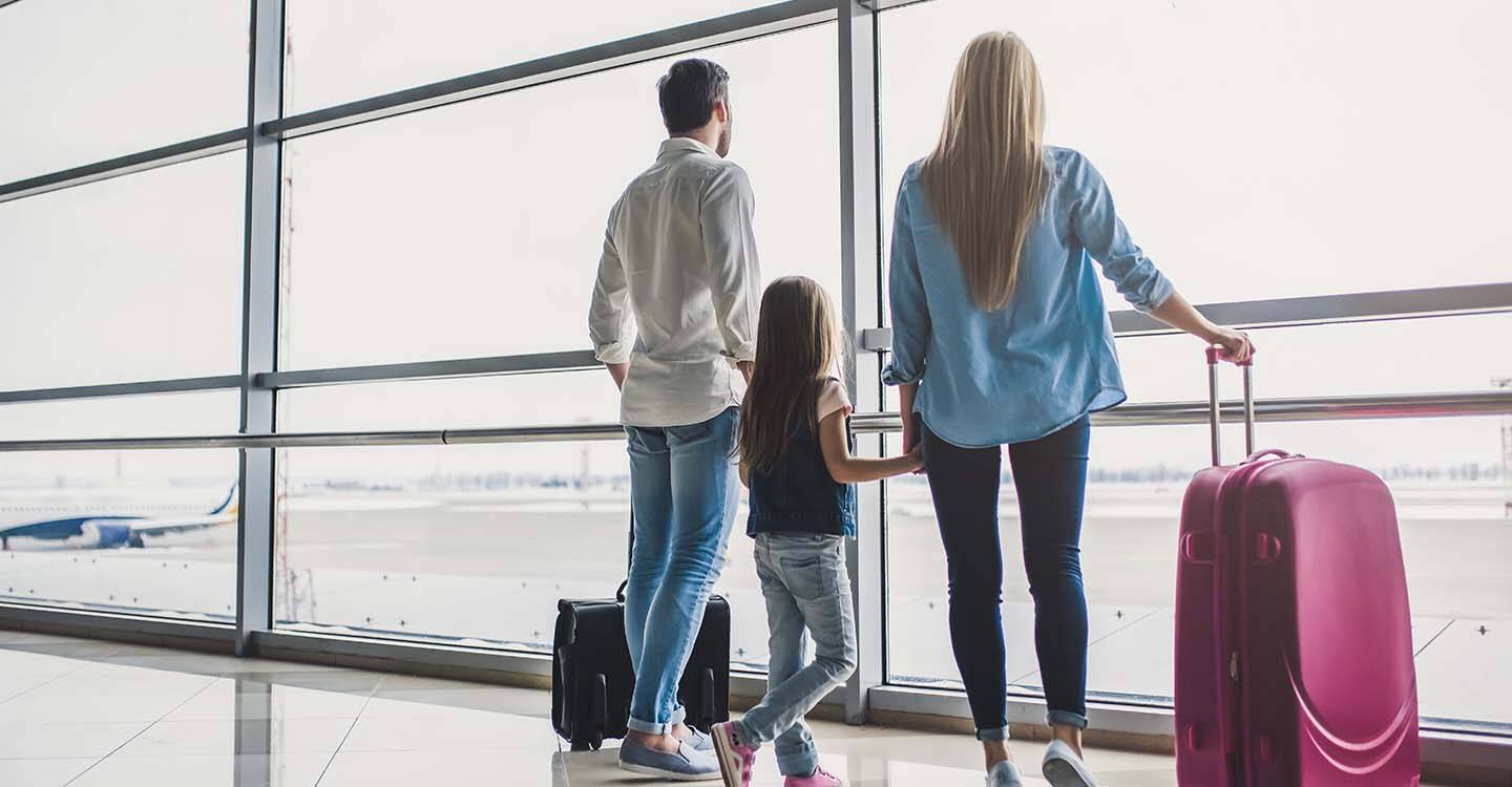 Familie mit Reisegepäck beobachtet am Flughafen Flugzeuge durch große Fensterfront