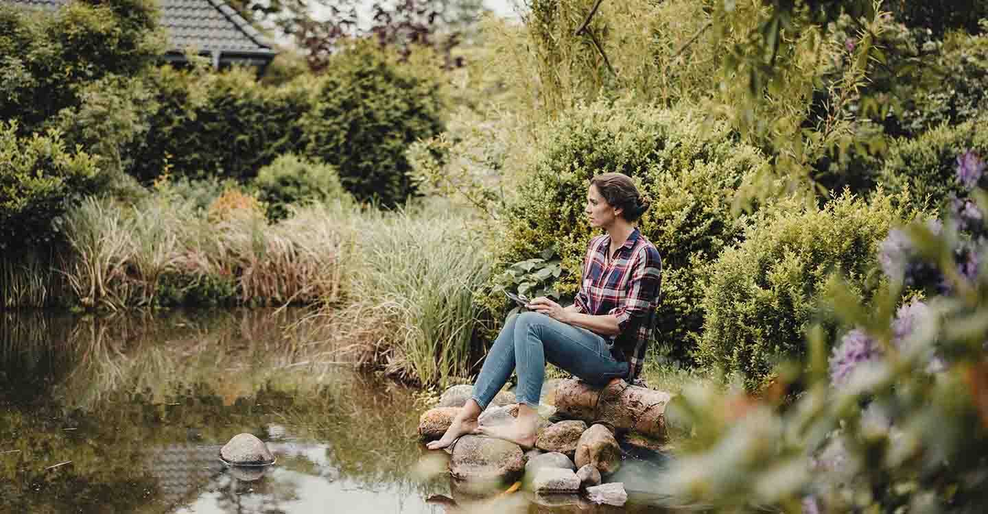 Frau sitzt am Wasser auf einem Baumstamm