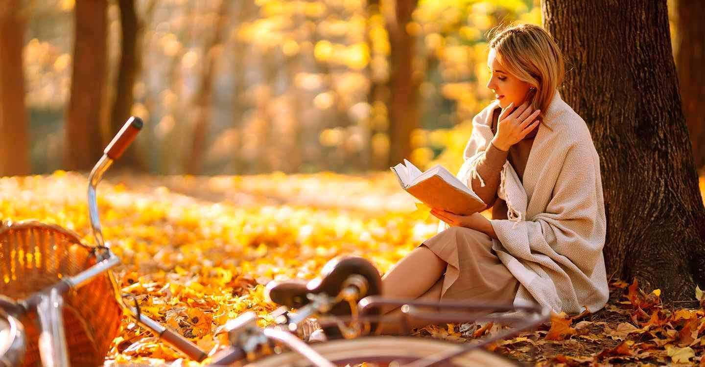 Eine Frau sitzt im Wald an einem Baum ein Buch lesend