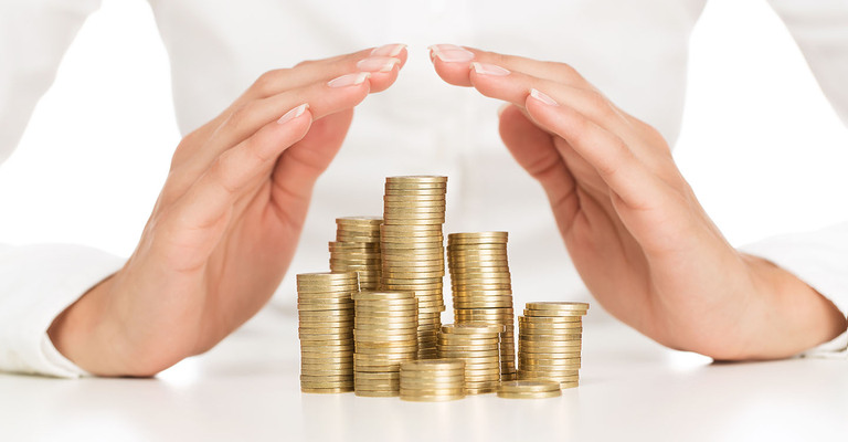 Frau hält Hände schützend über einige kleine Türme von Münzen