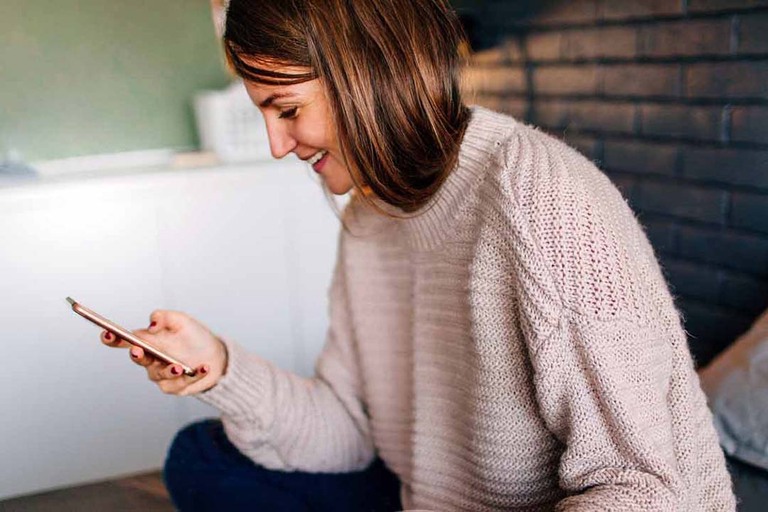 Frau sitzt mit dem Handy in der Hand auf einem Bett