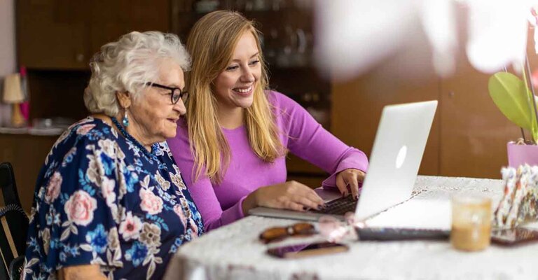 Erwachsene Enkeltochter hilft ihrer Oma bei der Nutzung des Laptops