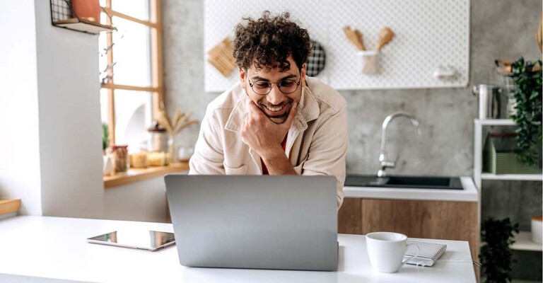 Ein junger Mann schaut lächelnd auf seinen Laptop