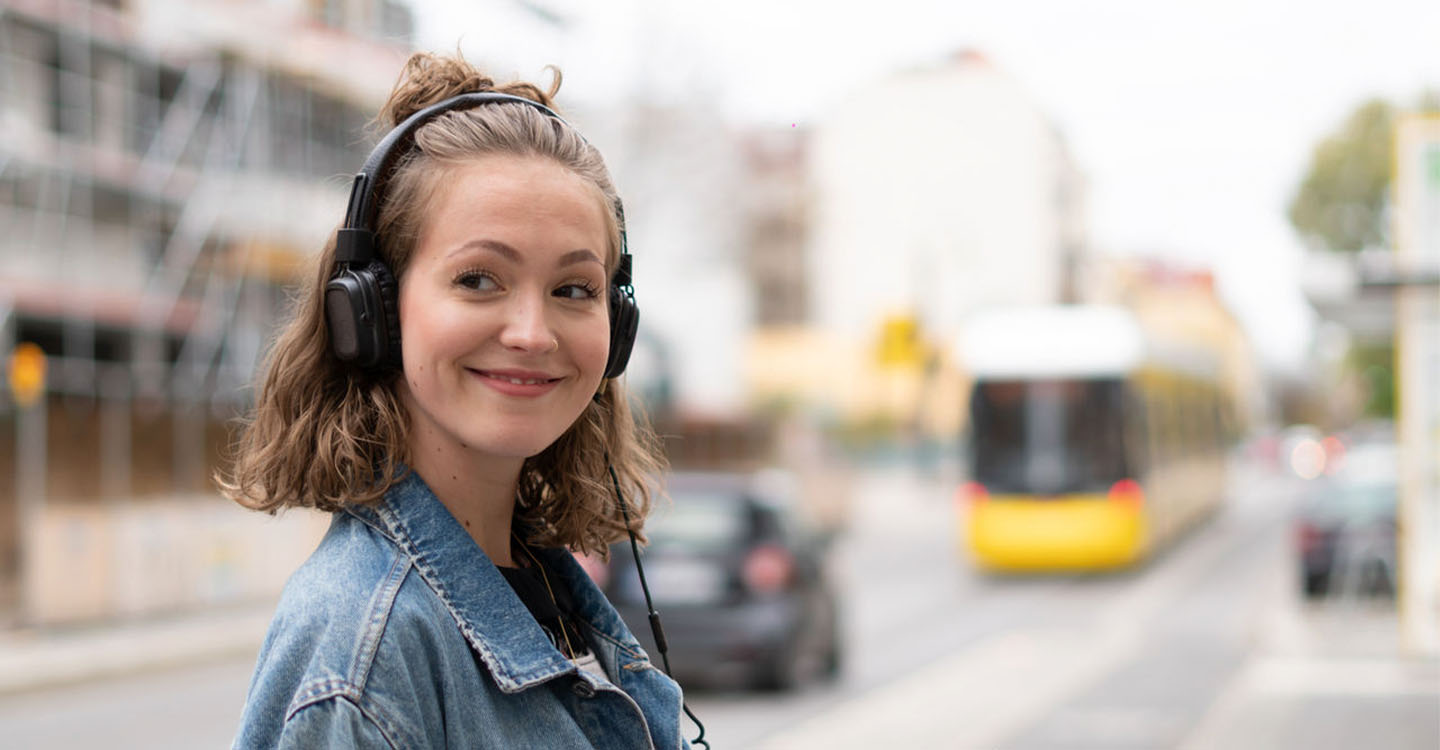Lena-mit-Kopfhörern-vor-einem-unscharfen-Hintergrund-mit-Strassenbahn