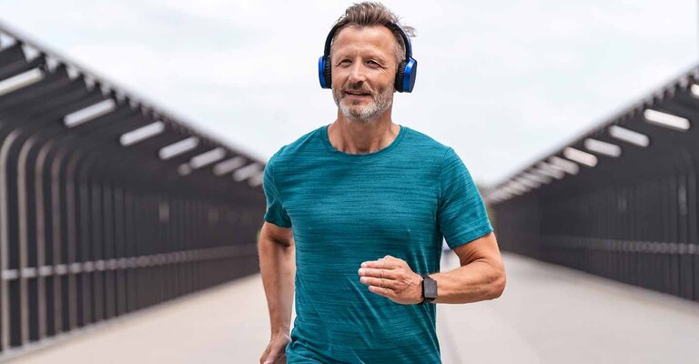 Mann in Sportkleidung mit Kopfhörern joggt über eine Straße