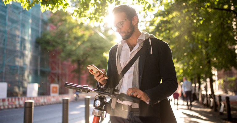 Mann mit E-Scooter und Smartphone im Sonnenlicht