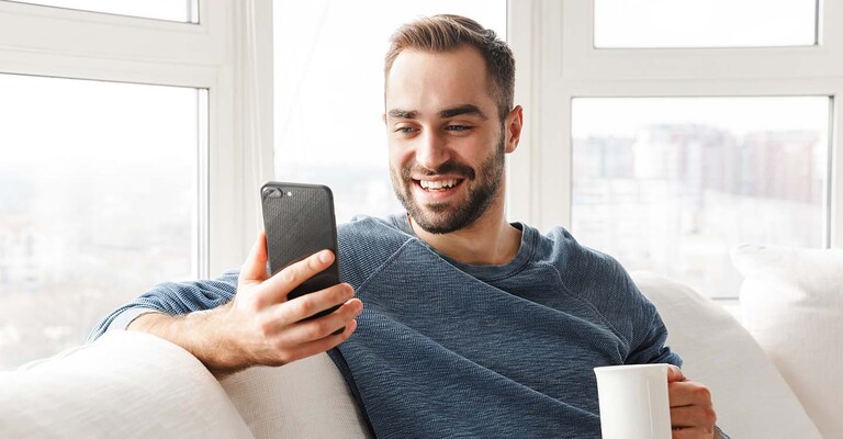 Mann mit Kaffeetasse schaut auf sein Smartphone