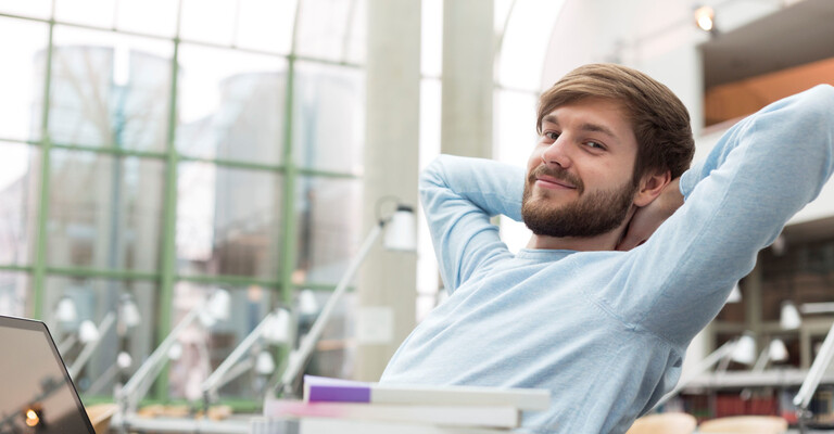 Mann sitzt zurückgelehnt entspannt auf einem Bürostuhl und schaut in die Kamera