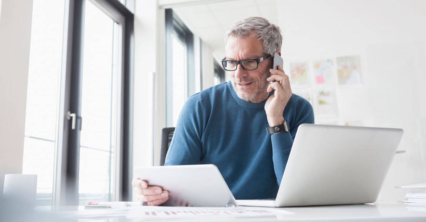 Mann telefoniert mit seinem Smartphone am Laptop