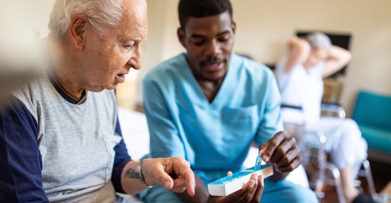 Pfleger erklärt einem Senior die Tablettendosis