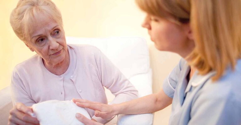 Pflegerin erklärt älterer Frau ein Hilfsmittel