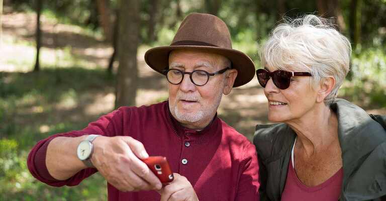 Älteres Paar im Wald schaut auf ein Smartphone