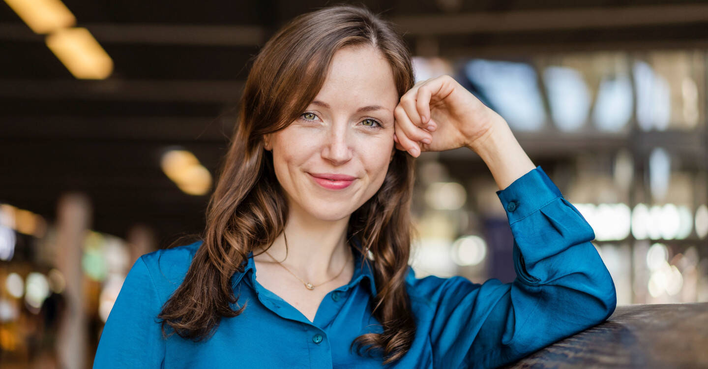 Lächelnde Frau mit blauer Bluse lehnt an einer Wand