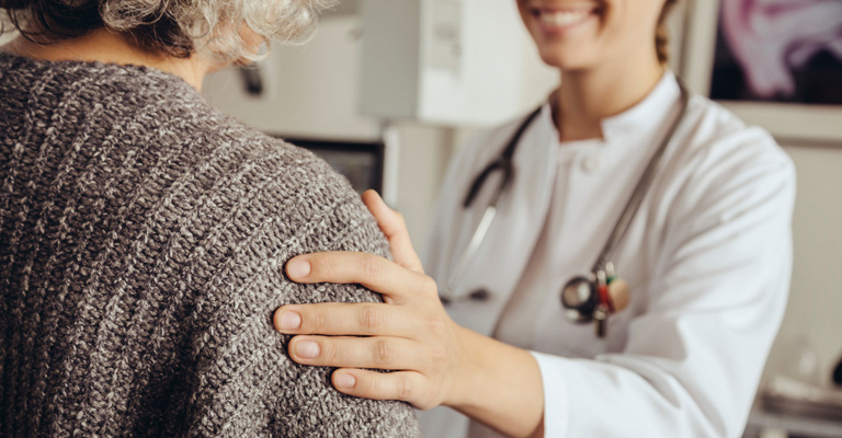 Ärztin legt Patienten Hand auf den Oberarm und lächelt ihn an